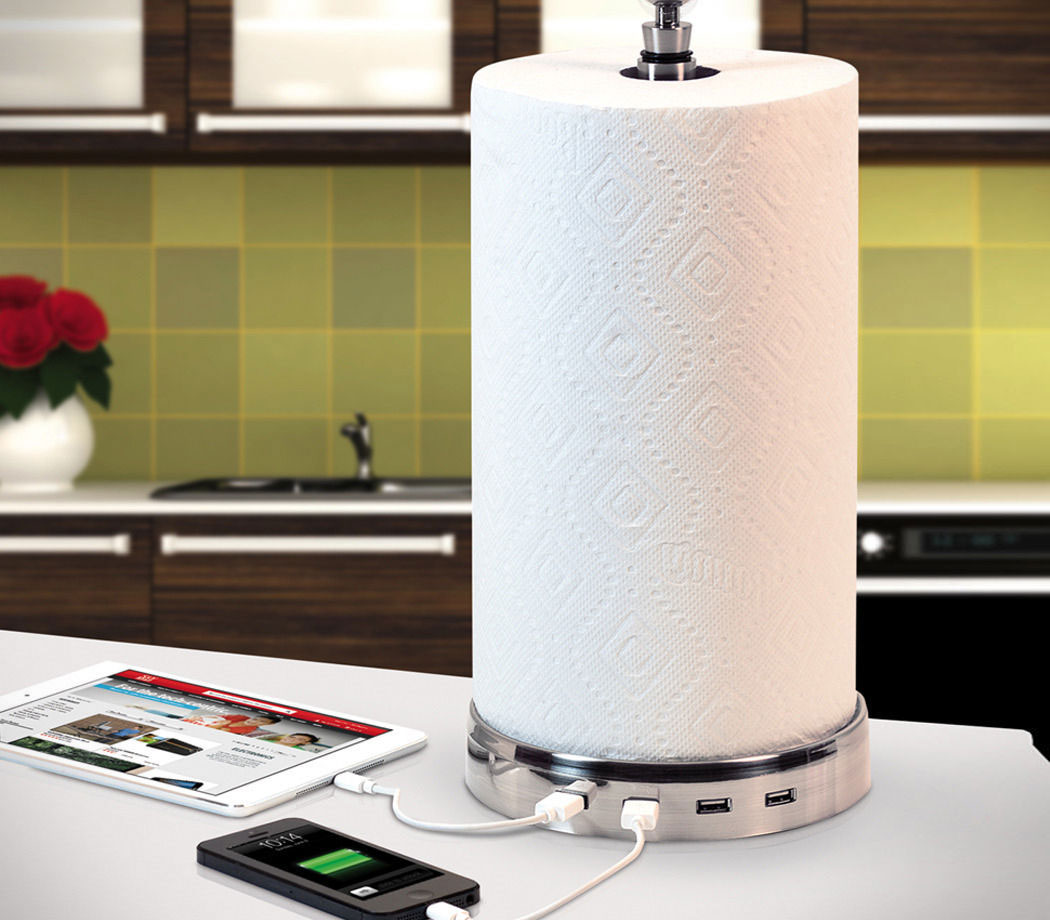 A promotional photo of a paper towel holder with four USB ports in the base. One port has a tablet plugged into it and one has a smartphone.